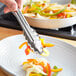 Choice stainless steel utility tongs holding food over a plate.