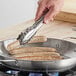 A person using Choice stainless steel utility tongs to cook sausages in a pan.