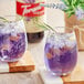 A glass of Torani lavender flavoring syrup with purple liquid, ice, and a sprig of rosemary.