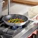 A person cooking food in a Choice aluminum non-stick fry pan on a stove.