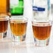 A group of Libbey shot glasses with brown liquid on a table.