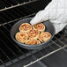 A hand using a Chicago Metallic Deep Dish Pizza Pan to hold cinnamon rolls.