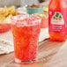 A glass of Jarritos Fruit Punch soda with ice on a table with a bottle of Jarritos orange soda and a plate of chips.