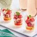Clear plastic Choice shot glasses filled with watermelon and feta cheese on a table at a catering event.