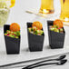 A group of Choice black plastic mini angled appetizer cups with food in them.