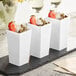 A group of white Choice square plastic mini cups with strawberries and nuts inside.