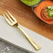 A Visions gold plastic tasting fork next to a plate of food.