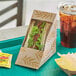 A World Centric sandwich wedge container with a sandwich, potato chips, and a drink inside.