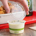 A hand holding a World Centric clear compostable plastic lid over a container of food.