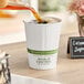 A cup of coffee being poured into a white World Centric compostable paper hot cup.