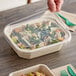 A hand holding a World Centric clear plastic container of salad with a green fork.