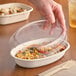 A hand placing a World Centric clear plastic lid on a white container of food.