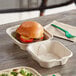 A World Centric compostable fiber clamshell burger box with a burger inside on a table.