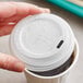 A hand holding a white World Centric travel lid on a coffee cup.