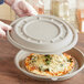 A person holding a pizza in a World Centric compostable fiber pizza container.