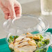 A hand holding a World Centric clear plastic lid over a salad.