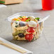 A World Centric clear plastic deli container of pasta and vegetables with a wooden fork 