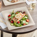 A World Centric compostable fiber plate with a salad and salmon on a table with a wooden fork and knife.