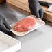 A hand in a black glove holding a piece of meat in a World Centric compostable fiber meat tray.