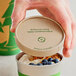 A hand holding a World Centric compostable paper container of yogurt with blueberries and granola.