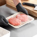 A person in black gloves holding a World Centric compostable fiber meat tray with raw hamburgers.