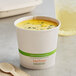 A World Centric compostable paper cup of soup with a wooden spoon.
