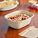 A World Centric compostable fiber container filled with food including meat and rice with a wooden fork on a napkin.
