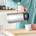 A man pouring coffee from a Bunn stainless steel thermal pitcher into a white mug.
