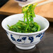 A Thunder Group Lotus melamine rice bowl filled with green seaweed on a table with chopsticks.