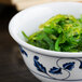 A Thunder Group Lotus melamine rice bowl filled with green seaweed.