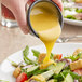 A person pouring Kraft Honey Mustard Dressing onto a salad.