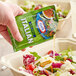 A hand pouring a Kraft Fat-Free Italian dressing packet into a salad.