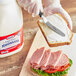 A person using a knife to spread Kraft Extra Heavy Mayonnaise on a sandwich.