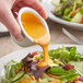 A person pouring Kraft Creamy French Dressing onto a salad.