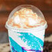 A clear Solo plastic dome lid on a cup of ice cream with whipped cream and caramel sauce.