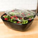 A Sabert black plastic catering bowl filled with salad on a counter.