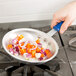 A hand using a Vollrath Wear-Ever fry pan to cook chopped vegetables on a counter.