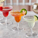 A group of Visions clear plastic mini margarita glasses with orange liquid and a green leaf on a table.
