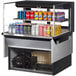 A Turbo Air black drop-in refrigerated display case with cans of soda and snacks on a shelf.