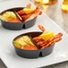 A Choice black plastic mini dual compartment dish with shrimp and sauce in each bowl on a table.