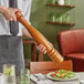 A person holding a wooden pepper mill over a plate of salad.