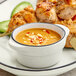A hand dipping chicken skewers into sauce in a grey matte stoneware sauce cup.