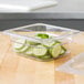 A clear plastic Cambro food pan with cucumber slices inside.