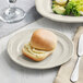 A sample Acopa Condesa scalloped wide rim porcelain plate with a sandwich and salad on it with a buttered roll.