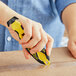 A person using a yellow and black Klever Kutter X-Change to cut a piece of cardboard.