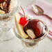 A dessert in a glass with Oringer Deluxe Hot Milk Fudge Topping, chocolate, and vanilla ice cream, and a cherry.