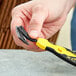 A hand holding a yellow and black Klever X-Change Wide Head Blade with Tape Splitter.