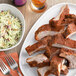 A plate of ribs and coleslaw with a piece of meat on a white plate.