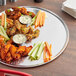 An 18" round aluminum platter with chicken wings and vegetables.
