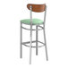 A Lancaster Table & Seating bar stool with a seafoam vinyl seat and antique walnut wood back.